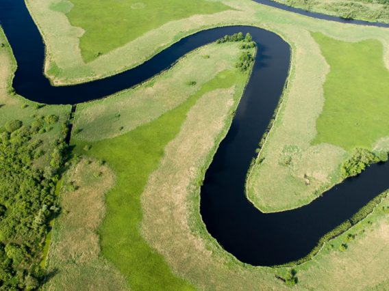 An aerial shot of a flooded river system. The surrounding land green and fertile.
