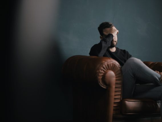 A man holding his head on a sofa.