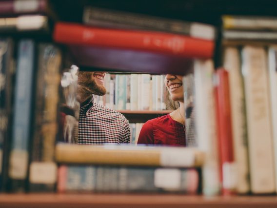 A window like gap in the shelves of a library reveals two women.