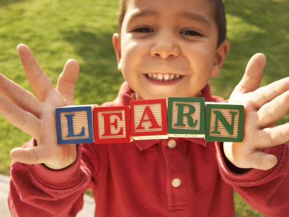 A smiling child holding up building blocks spelling out learn