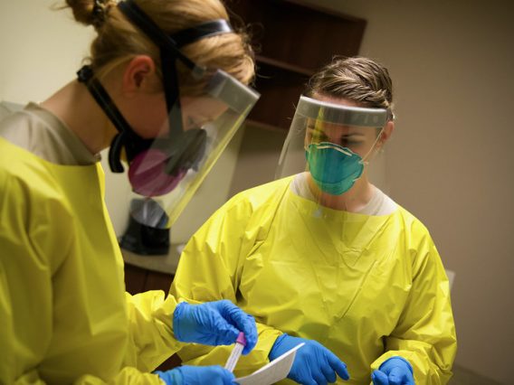 Two healthcare workers in full protective equipment conducting COVID-19 testing at log term care facilities